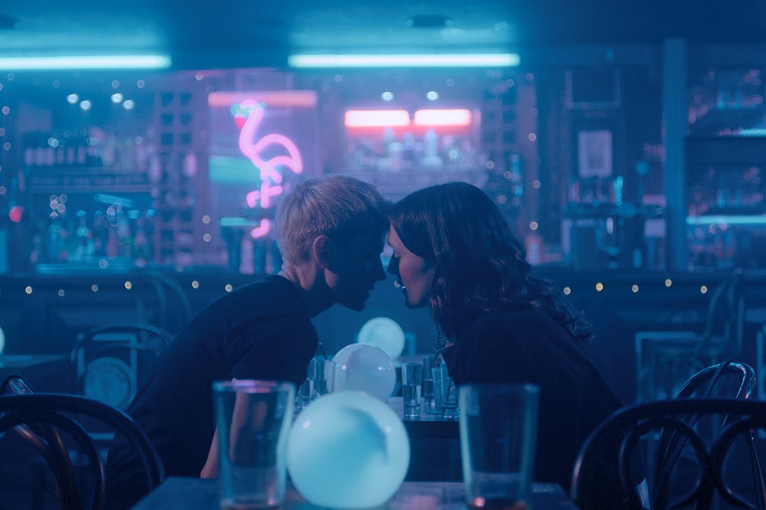 two young women hang their heads close together over a table in a diner.